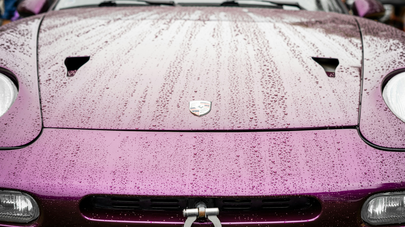 Hood of a maroon sports car with water-beading properties.